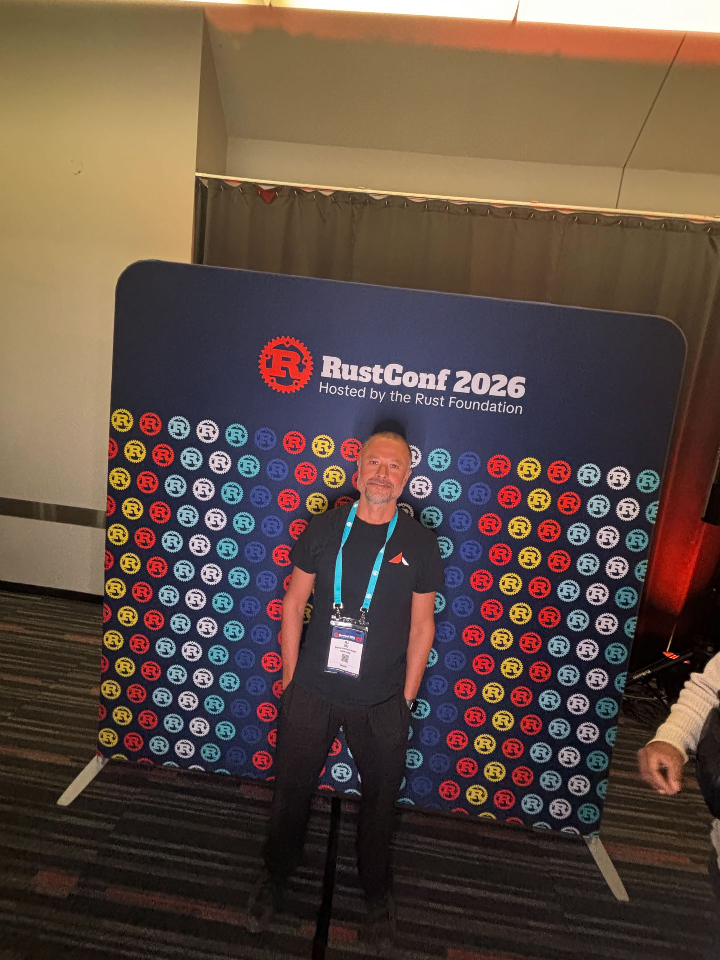 RustConf 2026 — MJ in front of the RustConf 2026 photo backdrop.