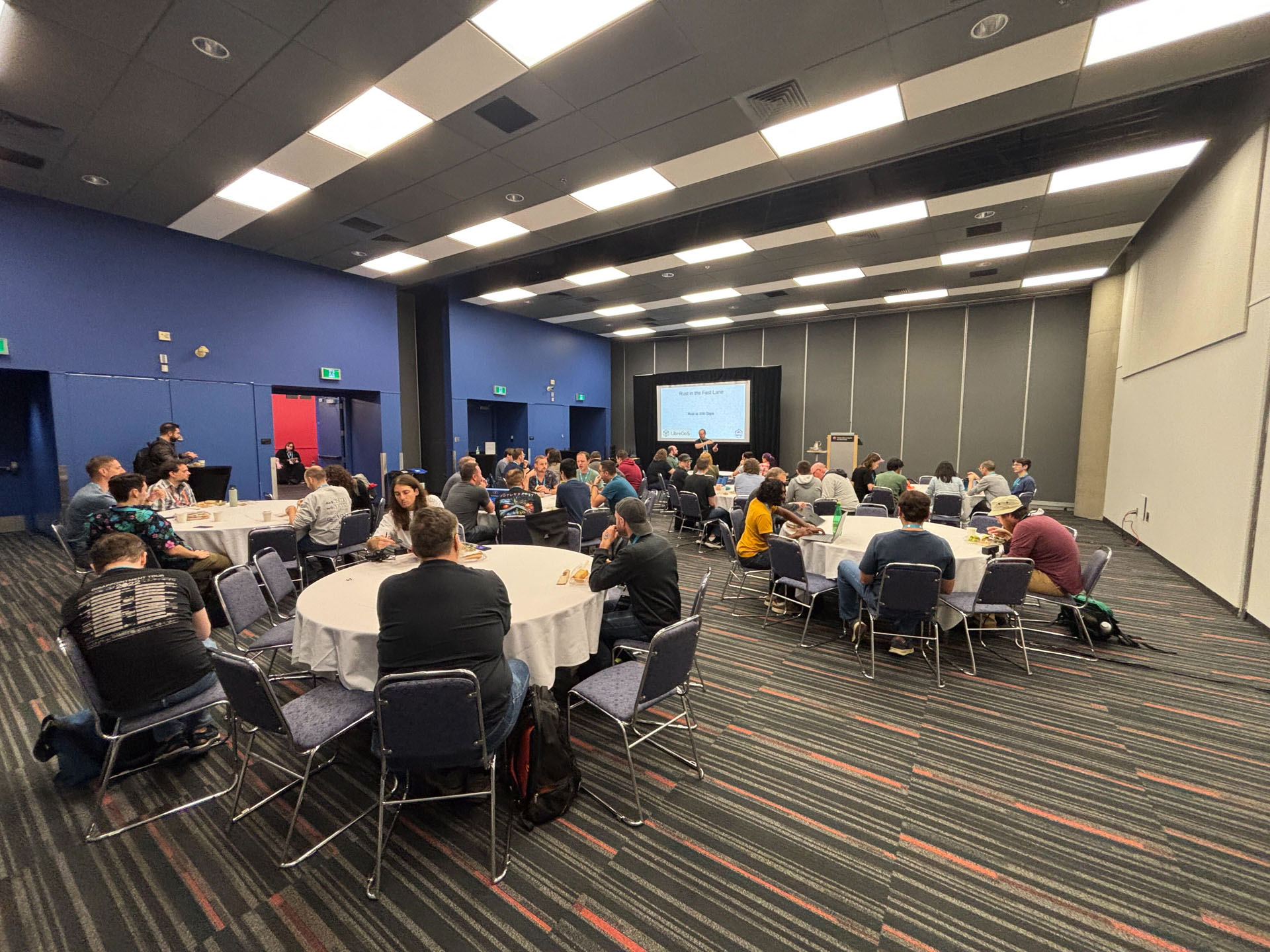 RustConf 2026 — attendees seated at round tables for a community room talk.