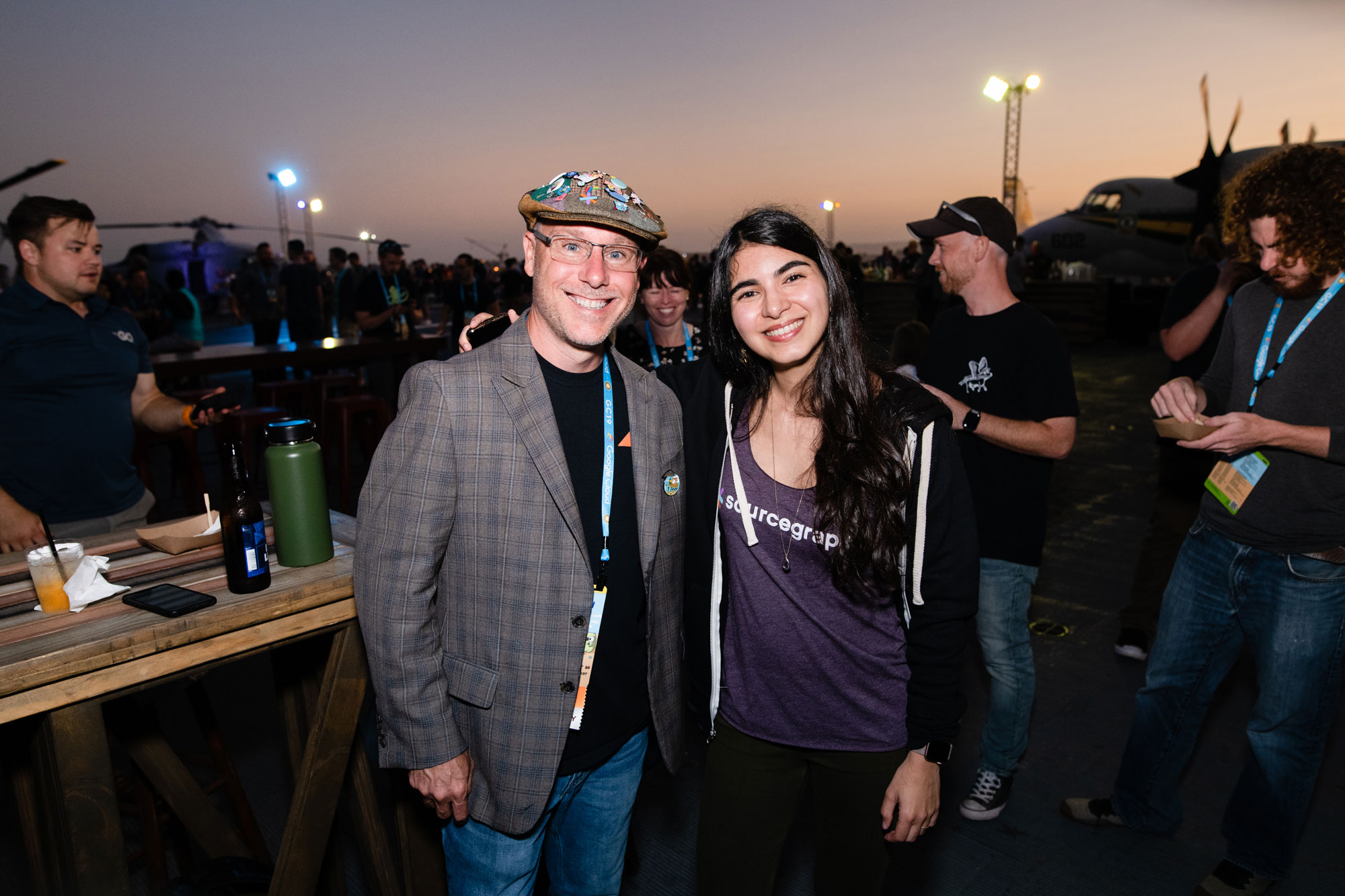 Evening outdoor conference social: attendees smiling and chatting near a lit aircraft in the background